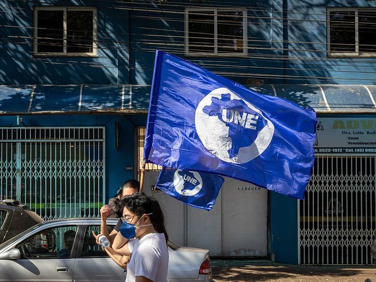 manifestantes da uniã nacional dos estudantes com bandeira da isntituição e máscaras pff2 azuis