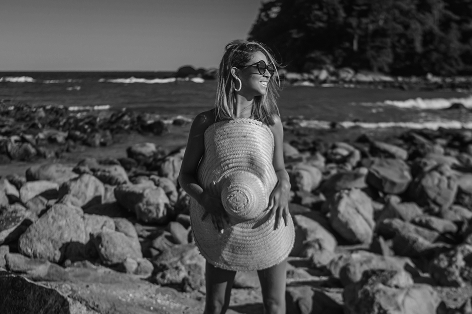 Foto em preto e branco Manuela Aguiar na praia, tampando seu corpo com um chapéu de palha