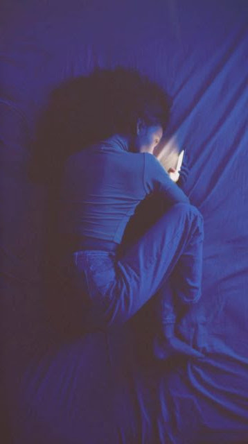 foto de menina em posição fetal na cama com celular na mão