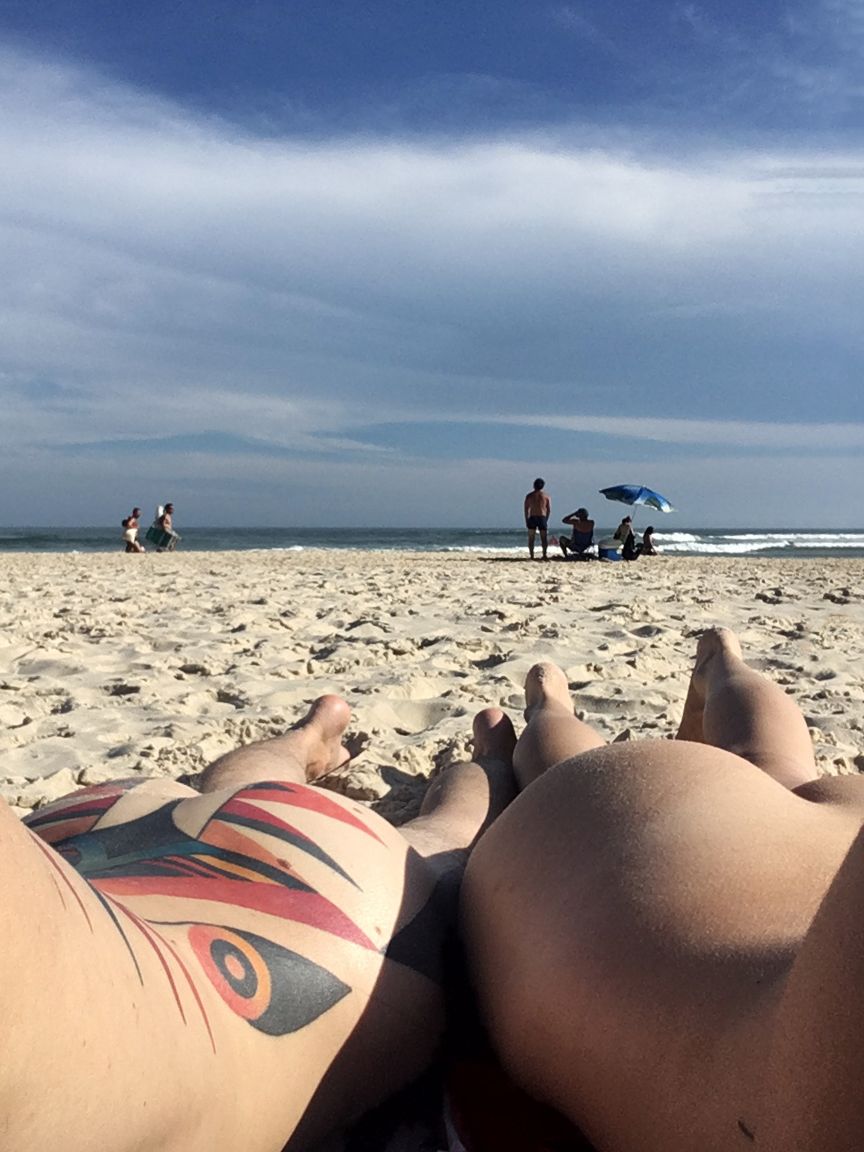 foto de duas pessoas nuas tomando sol de costas na praia